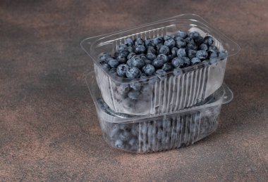 Kahverengi arka planda plastik kaplarda taze yaban mersini, dondurucu soğuğa hazırlanıyor.