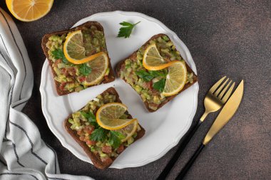 Ev yapımı Guacamole sandviçleri. Beyaz tabakta limonla süslenmiş. Kahverengi masada.