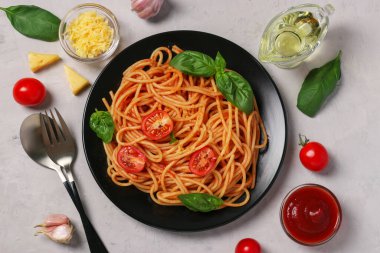 Domates soslu spagetti ve gri arka planda siyah tabakta fesleğenli kiraz domatesleri.