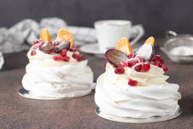 Kahverengi zemin üzerinde nar, mandalina ve üzümlü mini Pavlova keki, yakın plan.
