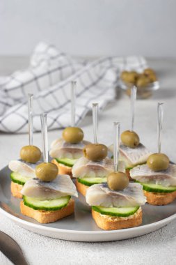 Tuzlu ringa balığı, zeytin ve salatalıklı beyaz ekmek tostlu gri arkaplan.