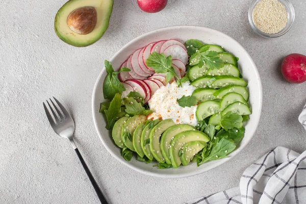 Stock image Salad with cucumbers, avocado, radishes and arugula, dressing with sour cream in white salad bowl, Top view