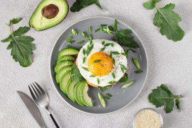 Jambonlu ev yapımı sandviç, yağda yumurta ve avokado kahvaltıda gri bir tabakta.