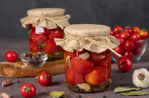 褐色背景的两个玻璃瓶中夹大蒜的腌制樱桃西红柿 冬季用 — 图库照片