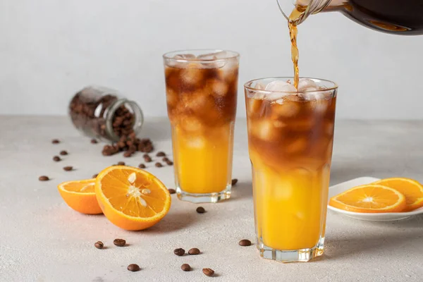 stock image Bumble coffee with ice on light gray background. Cold coffee is poured into a glass with orange juice and syrup