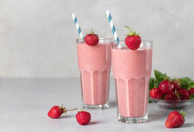 İki bardakta çilekli ev yapımı milkshake, gri arka planda pipet içmek, boşluğu kopyalamak.