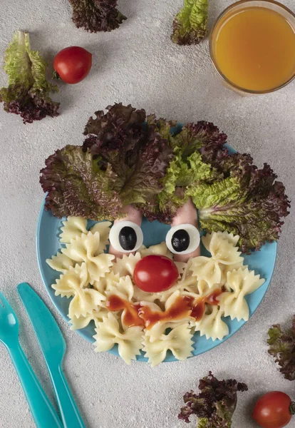 stock image Fun Food for kids - smiling face from pasta, sausages, egg, cherry tomato and lettuce leaves on blue plate, Top view