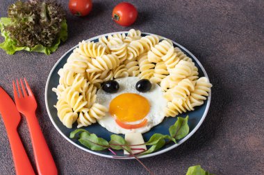 Çocuklar için eğlenceli yemek - kızarmış yumurta, makarna fusille, zeytin ve kahverengi masada pancar yapraklarından gülen yüz