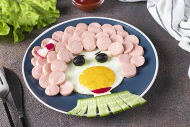 Çocuklar için eğlenceli yiyecekler - kızarmış yumurta, sosis, zeytin ve mavi tabakta salatalık gibi gülen yüzler. Çocuklar için yaratıcı, sağlıklı bir kahvaltı.
