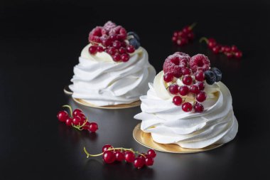 Mini Pavlova cake with raspberry, blueberry and red currant on black background