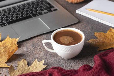 Kahve, dizüstü bilgisayar ve defter, sonbahar yapraklarının yanındaki kahverengi masa, evde çalışma kavramı.