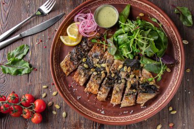 Ahşap masada soslu, soğanlı, limonlu ve yeşil salatalı ızgara uskumru.