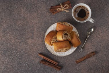 Kahverengi arka planda bir fincan kahvenin yanında tarçınlı rulo, Üst Manzara