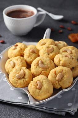 Ev yapımı havuç kurabiyeleri, kaju fıstığı ve kurutulmuş kayısılar ve gri arka planda bir fincan kahve, dikey görüntü.