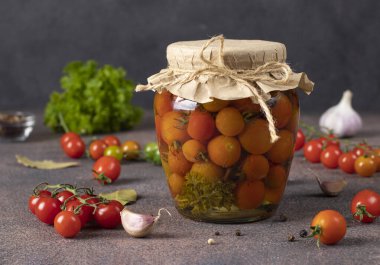 Kahverengi masadaki cam kavanozda sarımsaklı vişneli domates turşusu.