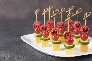 Vişneli domates, sosis, peynir ve salatalıkla beyaz tabakta kaplan.