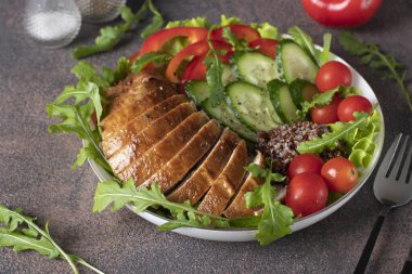 Fırında tavuk göğsü, kinoa, kiraz domatesleri, salatalık, dolmalık biber, marul yaprağı ve roka kahverengi masada, yakın plan.