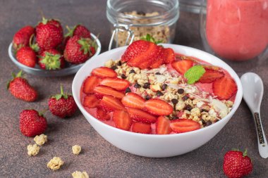 Kahverengi arka planda çilek, granola, badem ve çikolatalı sağlıklı kahvaltı smoothie kasesi.