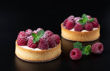 Siyah arkaplanda taze ahududu olan tartlar.