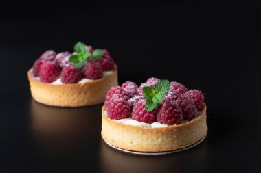 Siyah arkaplanda taze ahududu olan tartlar.