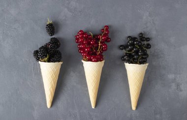 Gri arka planda böğürtlen ve üzümlü waffle külahları, yukarıdan görünüm