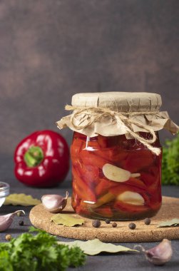 Pickled sweet peppers with garlic in glass jar on brown background