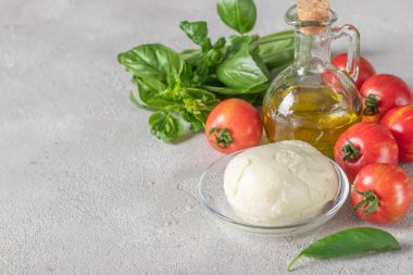 Caprese İtalyan salatası yapmak için gerekenler: domates, mozzarella peyniri, fesleğen ve açık gri arka planda zeytinyağı