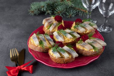 Tuzlu ringa balıklı, peynirli ve yumurtalı lezzetli sandviçler, gri arka planda pancar gülü ile süslenmiş.