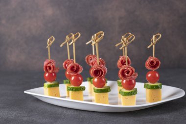 Beyaz tabakta kiraz domatesli, sosisli, peynirli ve salatalıklı kanepe