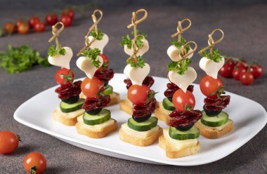 Peynirli kanepe, vişneli domates, sosis ve beyaz tabakta siyah zeytin.