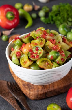 Acı biberli yeşil domates salatası ve tahta tahtadaki beyaz salata kasesinde sarımsak.