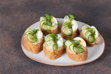 Kahverengi zemin üzerinde ton balıklı börek, yumurta ve salatalık.