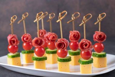 Vişneli domates, sosis, peynir ve salatalıkla beyaz tabakta kaplan.