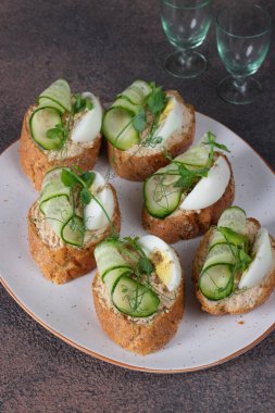 Beyaz tabakta ton balıklı börek, yumurta ve salatalık.