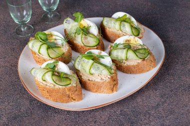 Kahverengi zemin üzerinde ton balıklı börek, yumurta ve salatalık.