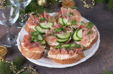 Krem peynirli sandviçler, jambon ve salatalık kahverengi arka planda beyaz tabakta.