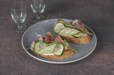 Krem peynirli sandviçler, jamon ve salatalık kahverengi arka planda gri tabakta.