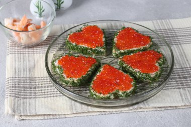 Yuvarlak tabakta kırmızı havyar ve gri arka planda kupa şekli, Sevgililer Günü kahvaltı fikri.