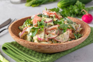 Salatalıklı salata, turp, domates, haşlanmış yumurta ve otlar açık gri arka planda ahşap bir tabakta.