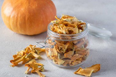 Açık gri arka planda cam kavanozda ev yapımı balkabağı cipsi..