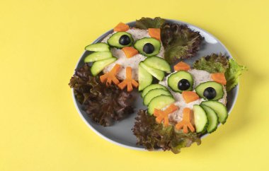 Sarı zemin üzerinde salatalıklı, havuçlu ve zeytinli çocuklar için baykuş şeklinde sandviçler