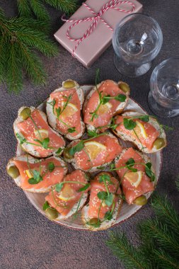 Kahverengi arka planda tuzlu somon, zeytin ve limonlu sandviçler.