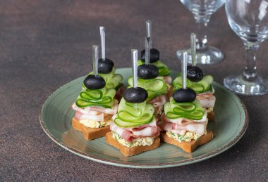 Pastırmalı kanepeler, salatalık ve yeşil tabakta kızarmış ekmek üzerine siyah zeytin.