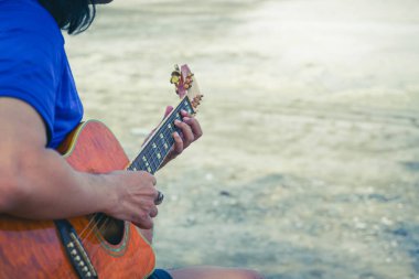 Sahilde dramatik bir tonda gitar çalan insan.