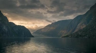 Timelapse video of sunset with last sunbeams in the fjord and mountain landscape Eidfjord in Norway, moving clouds in the sky and surface of water