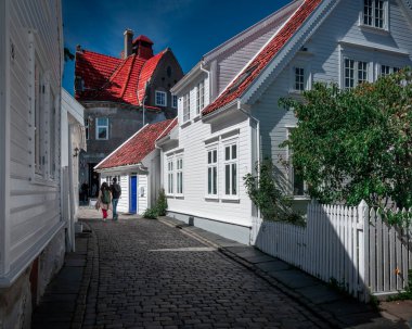 Couple walking through old town Gamle Stavanger with white timber houses in Norway, during sunshine and blue sky