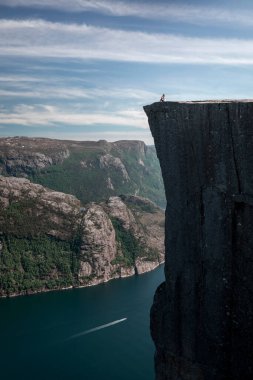 Woman sitting on the ridge of famous Preikestolen rock, with view into Lysefjord in Norway, water and boat under the steep cliff