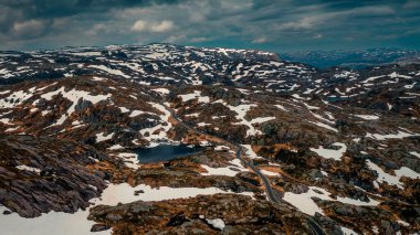 Landscape with lonesome road from above around Lysefjord in Rogaland with lakes and snow in Norway, dark cloudy sky