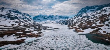Snowy landscape of Hardangervidda national park with mountains and a road along icy lakes in Norway, from above