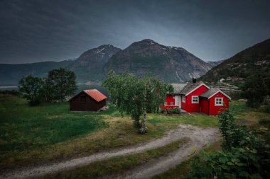 Red houses at the waterfront of small town of Eidfjord in Norway, surrounded by mountains of the fjord
